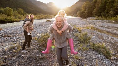 Grandfather and father carrying children piggyback at a riverbank at sunset