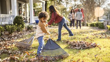Children raking leaves in front yard of home