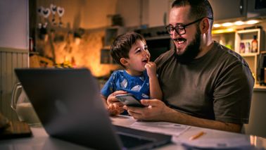 Young dad uses laptop and pays bills with son on lap 