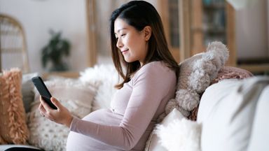 Woman sitting on coach and looking at phone researching short-term and long-term disability insurance 