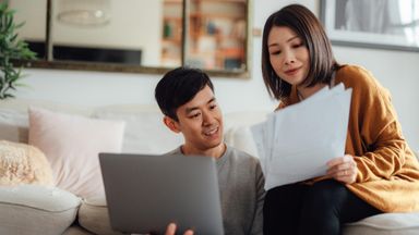 Young couple discussing financial bills while using laptop in living room.