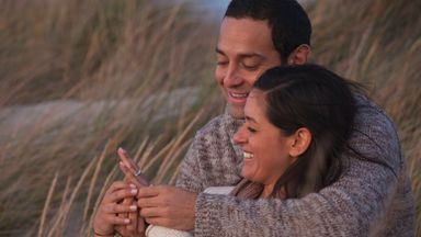 Couple sitting together smiling looking at an engagement ring
