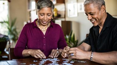 Two 60-year-olds assemble a puzzle at home.