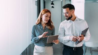 Shot of two coworkers having a discussion in modern office. Businessman and businesswoman in meeting using digital tablet and discussing business strategy. Confident business people working together in the office. Creative business persons discussing new project and sharing ideas in the workplace.