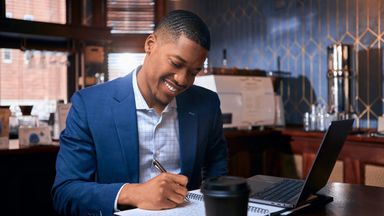Male advisor smiling and writing notes with laptop