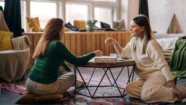 Two women are playing board games at a table inside a home. 