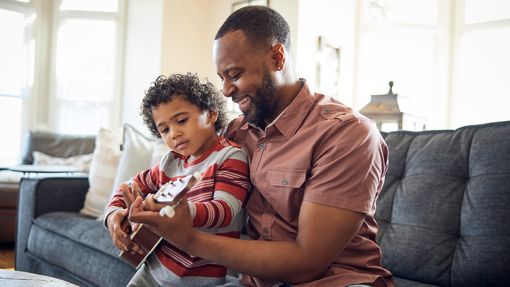 father and son playing ukulele on sofa