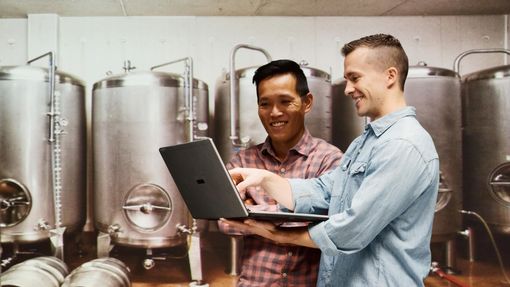 Two men discuss about disability insurance for self-employed on their laptop.