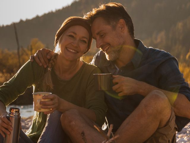 Happy couple camping and drinking coffee next to river