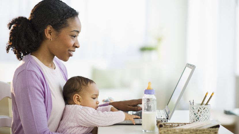 Mom working on a laptop with her baby deciding when to revisit her life insurance coverage.