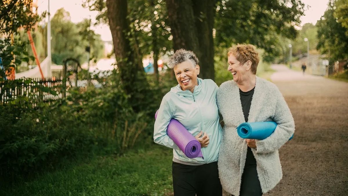  smiling female friends walking and holding exercise mats