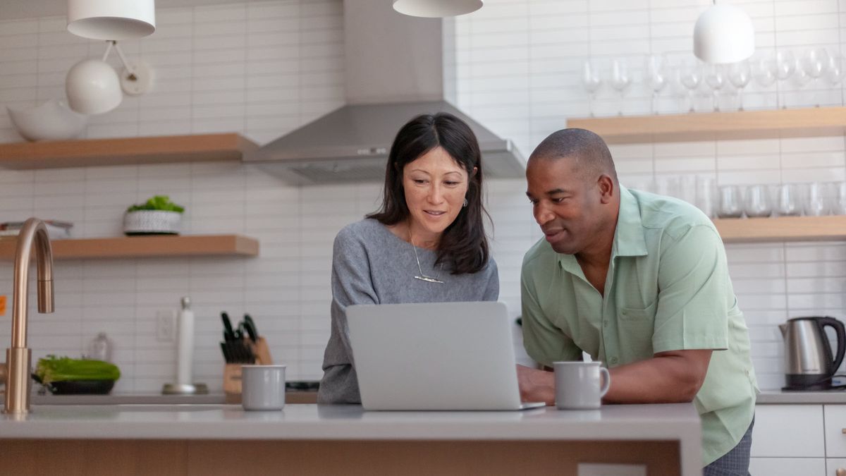 Husband and wife looking at a computer while standing in their kitchen thinking about smart moves for rising interest rates