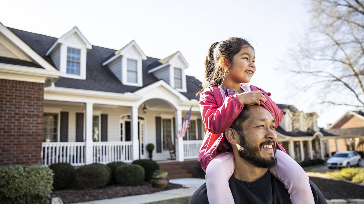 Man with his daughter on his shoulders outside a home