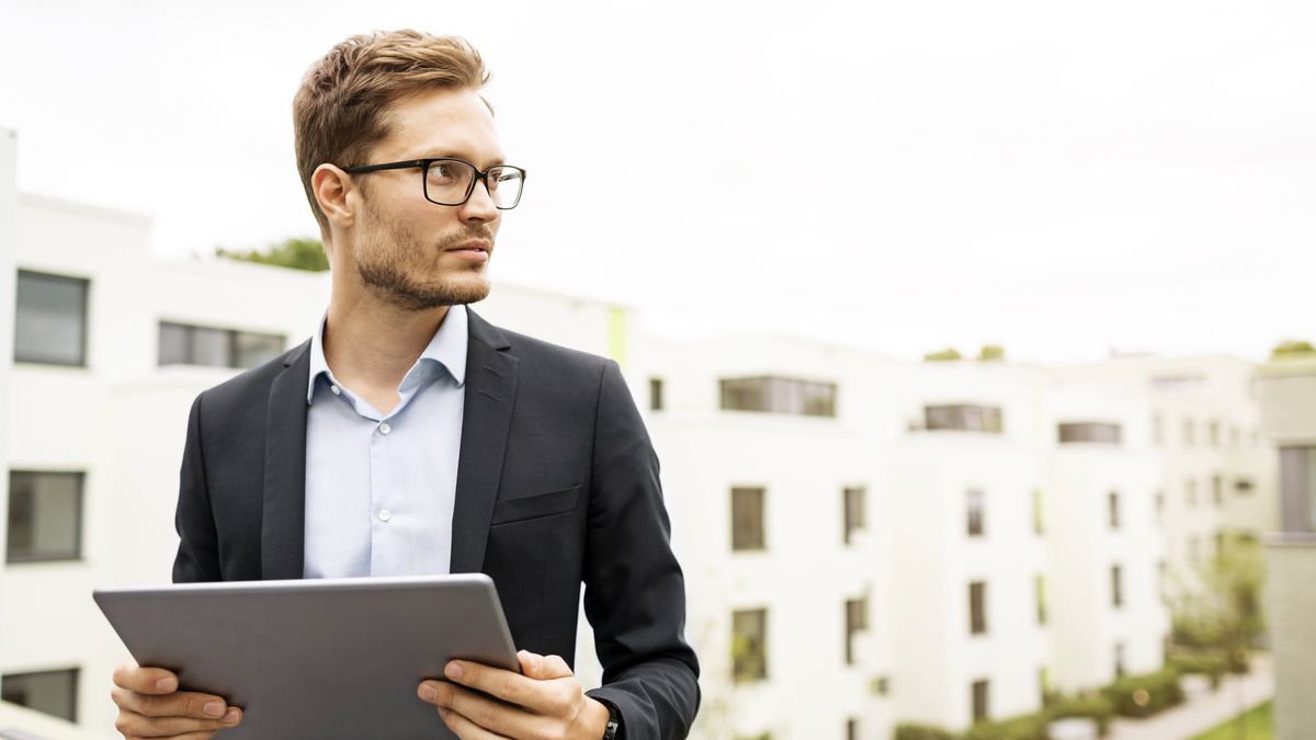 Man with a large tablet standing outside condos researching a real estate investment trust