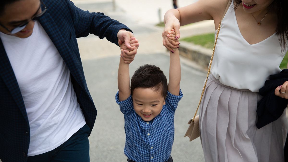 Mother and father holding their child by the arms as they walk with him and discuss custodial accounts.