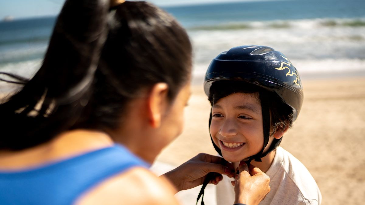 A parent helps a child with a sports helmet.