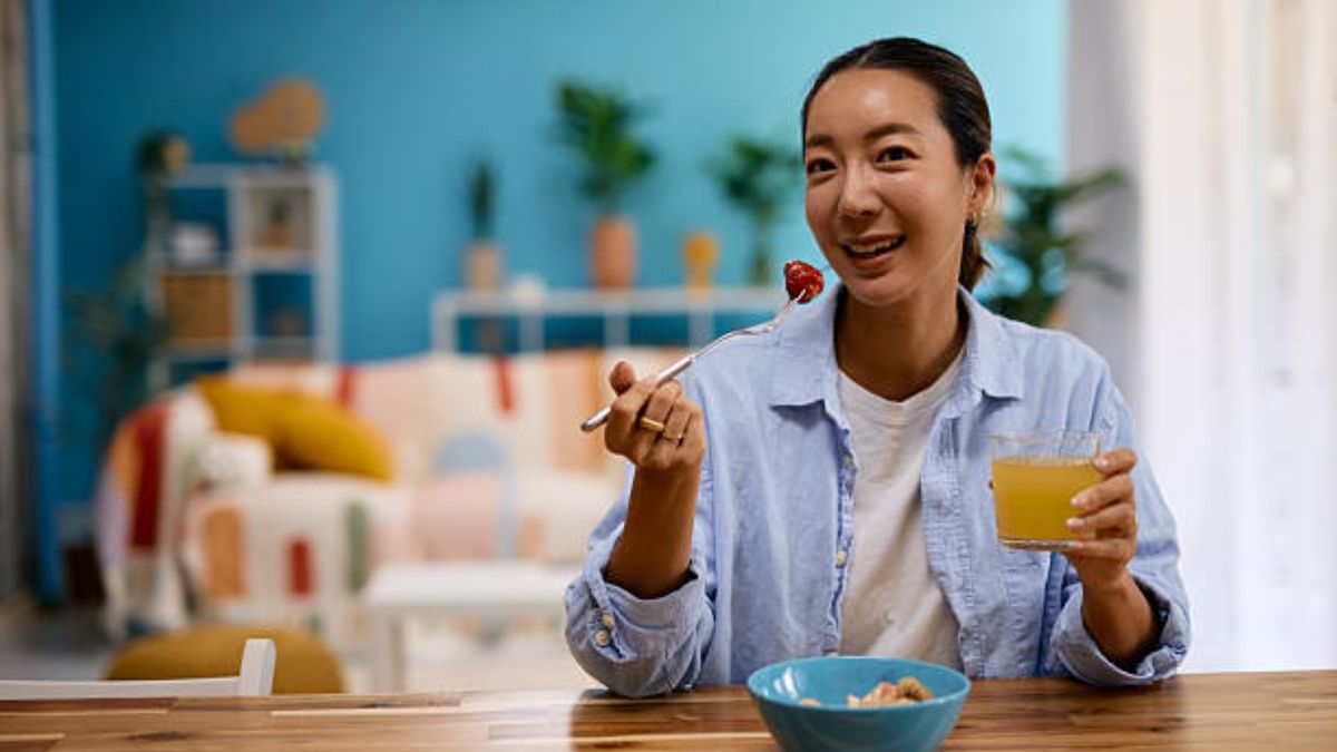 Young woman enjoying breakfast at home with fresh fruit and orange juice. 