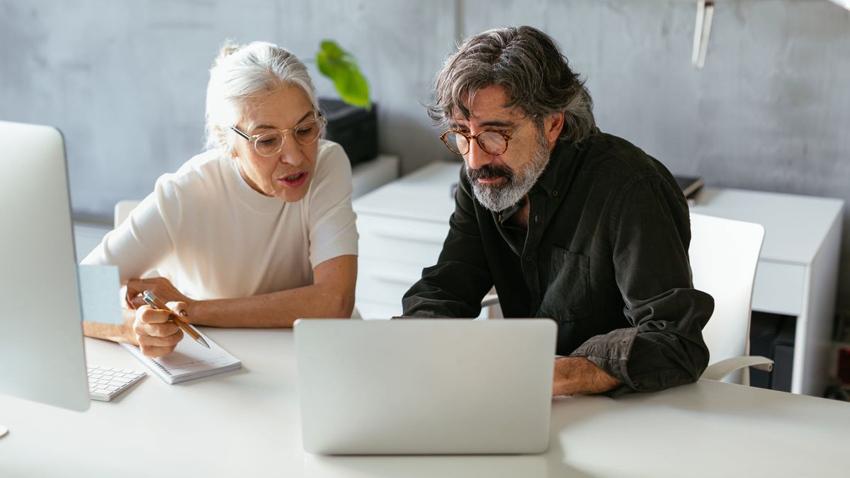 Two colleagues in modern office, reading information on laptops