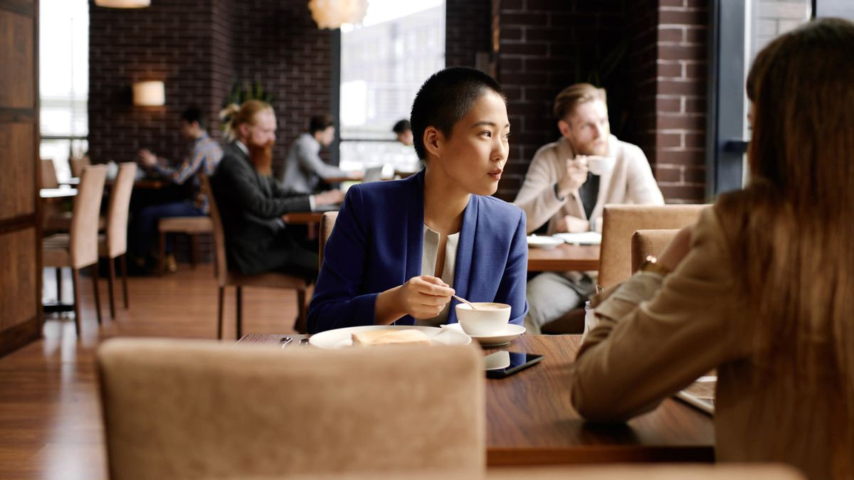 Businesswoman sitting at table in cozy cafe, stirring coffee and assessing the markets and economy white reading Northwestern Mutual’s Weekly Market Commentary