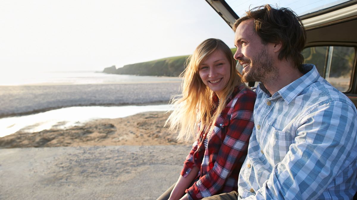 A couple chat and laugh whilst they sit in their car at the beach.