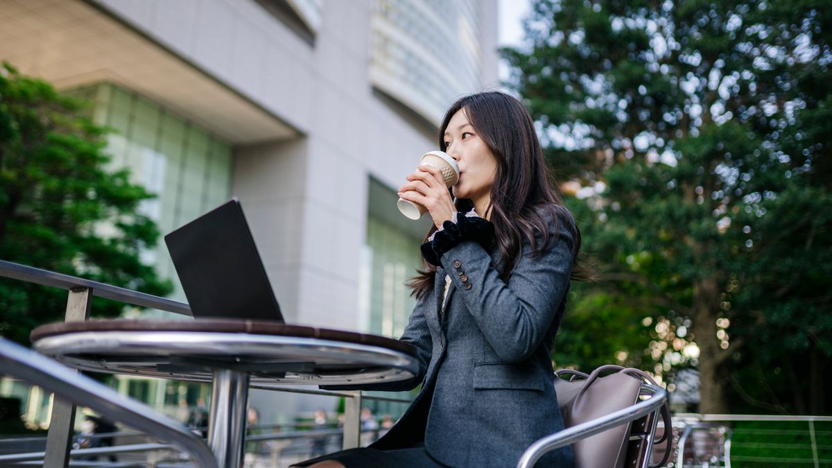 Businesswoman works on laptop outside modern office, analyzing markets and investments