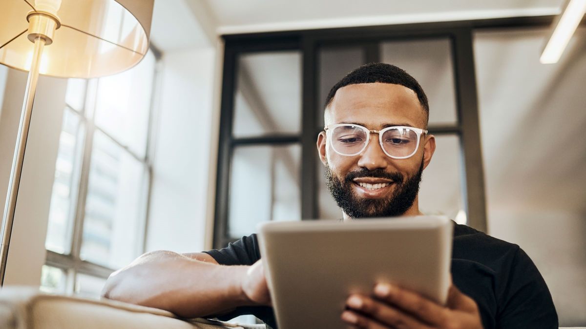 Young man sitting on sofa and reading Northwestern Mutual’s Weekly Market Commentary on his tablet.