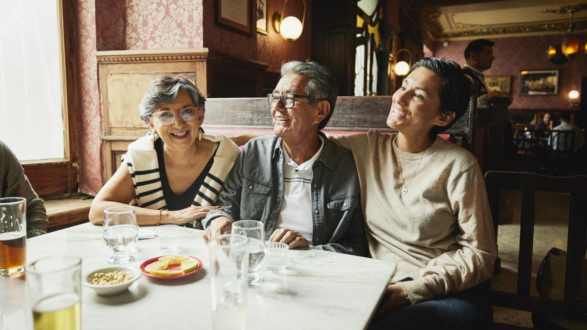 Smiling adult daughter and senior parents hanging out in booth in bar during city vacation.