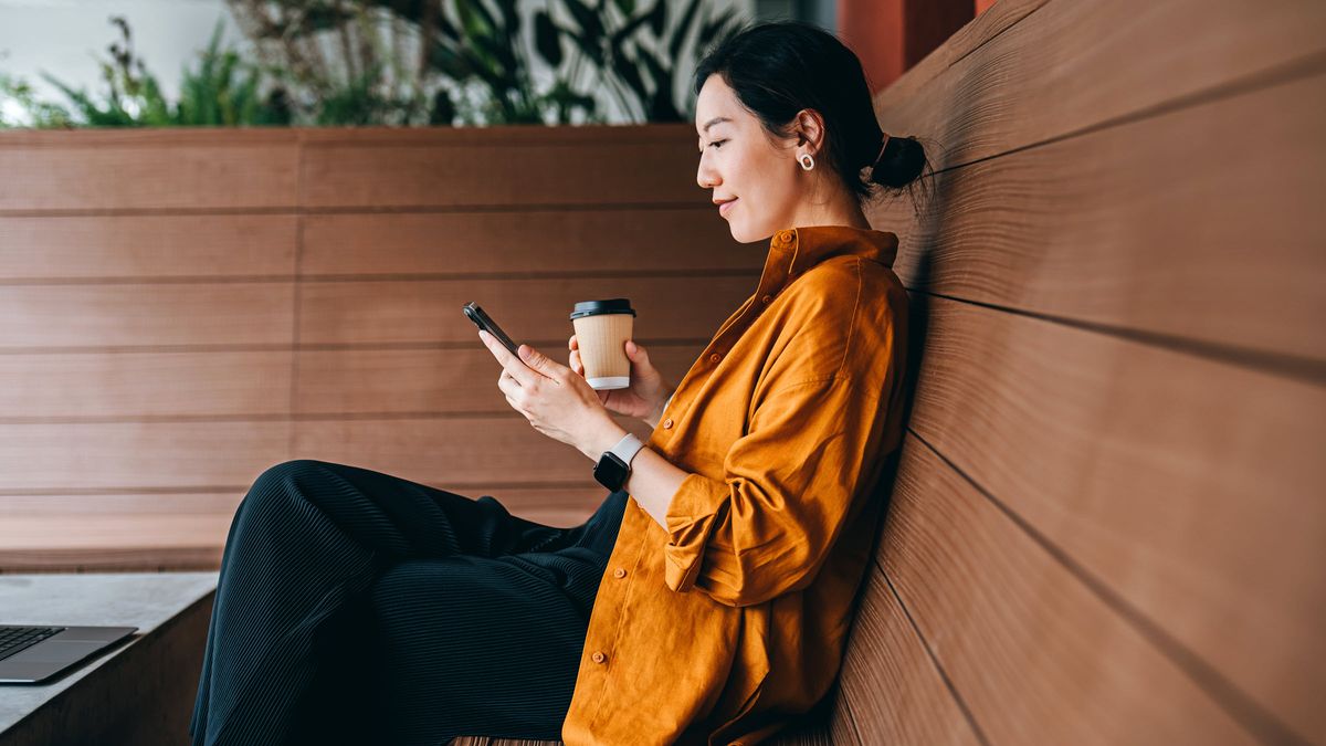 Young woman sitting in a sidewalk cafe with a cup of coffee and using her smartphone.