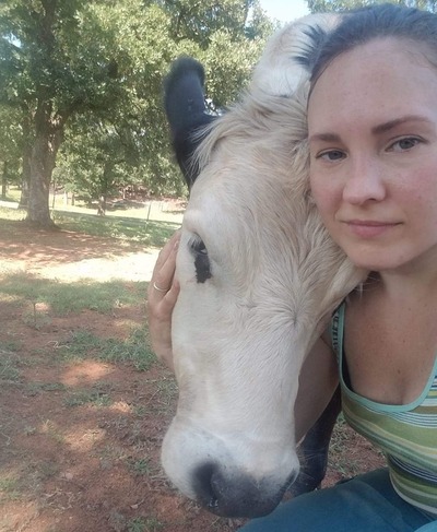 A woman cuddling a white cow with black ears.