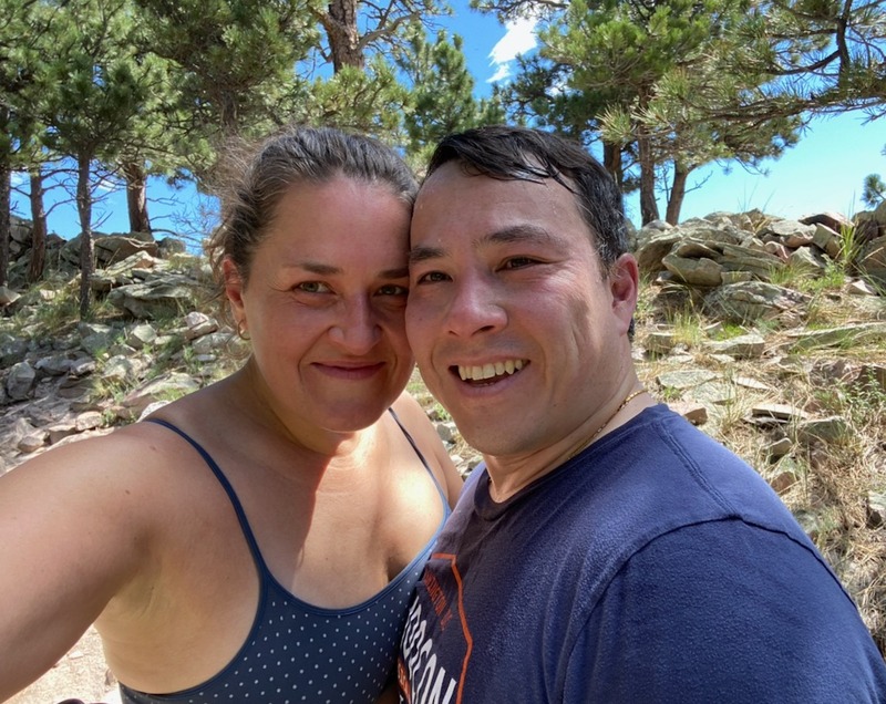 Blue skies and pine trees behind couple on a mountain