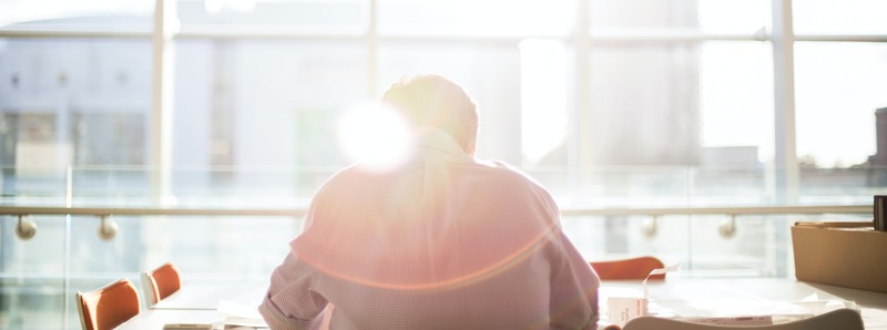 Technology professional with head bowed hard at work at their desk. The sun is streaming in through some windows.