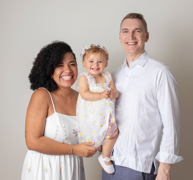 David's family. His wife in a white dress on the left, him holding their baby daughter in a white dress on the right.