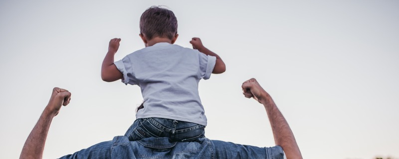 child sitting on fathers shoulders with power stance 
