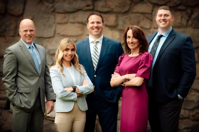 5 professionally dressed people standing in front of a stone backdrop