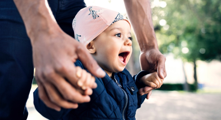 A parent holding a toddler's hands while they learn to walk